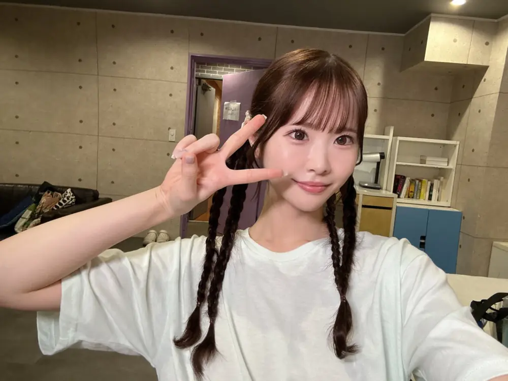 Emika Shirakami ถักผมเปียและชูสองนิ้วในเสื้อยืดสีขาว