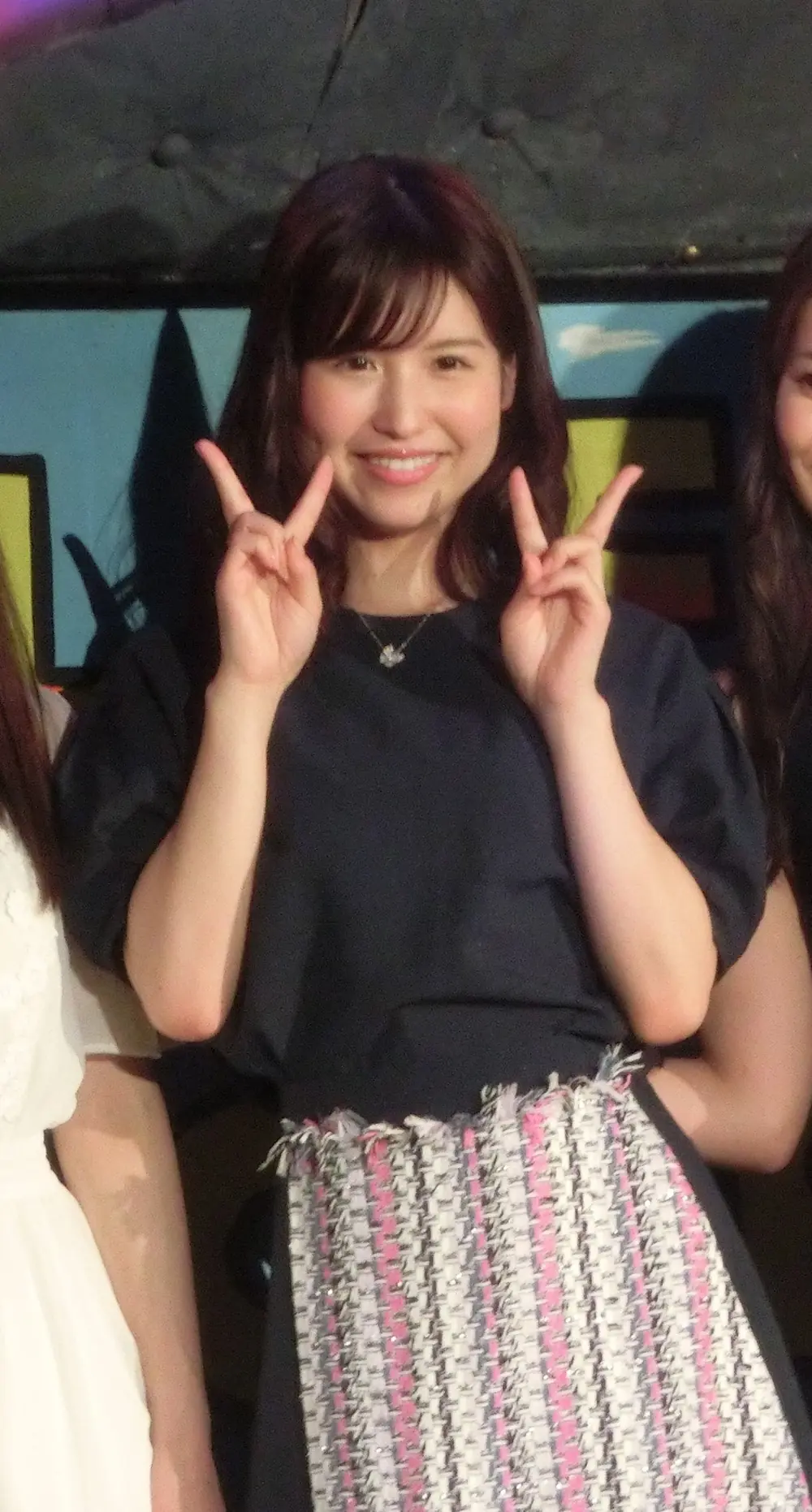 Momo Sakura สวมเสื้อสีดำกับกระโปรงลายและชูสองนิ้ว