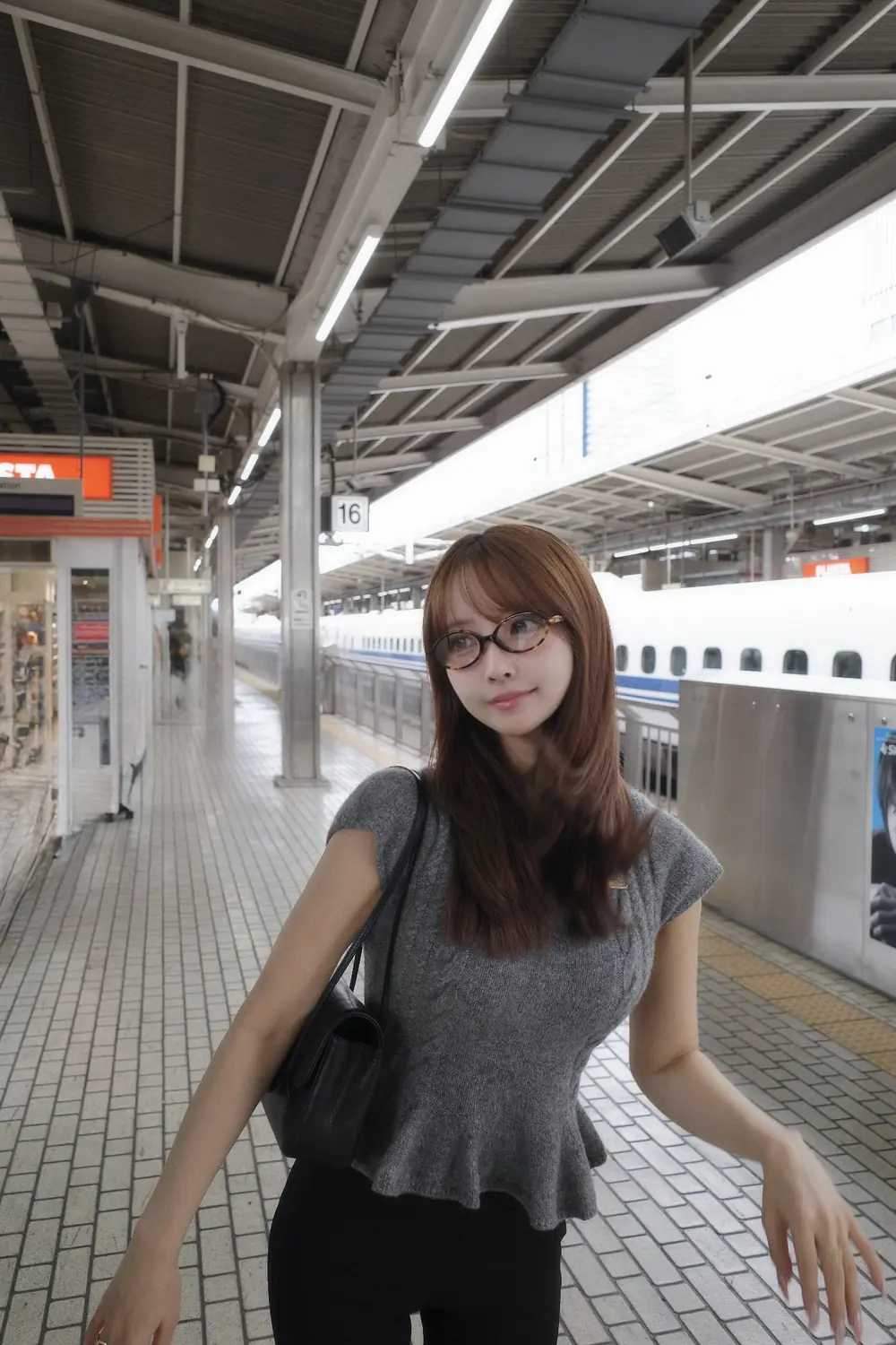 Yua Mikami สวมแว่นและเสื้อสีเทาบนชานชาลาสถานีรถไฟ