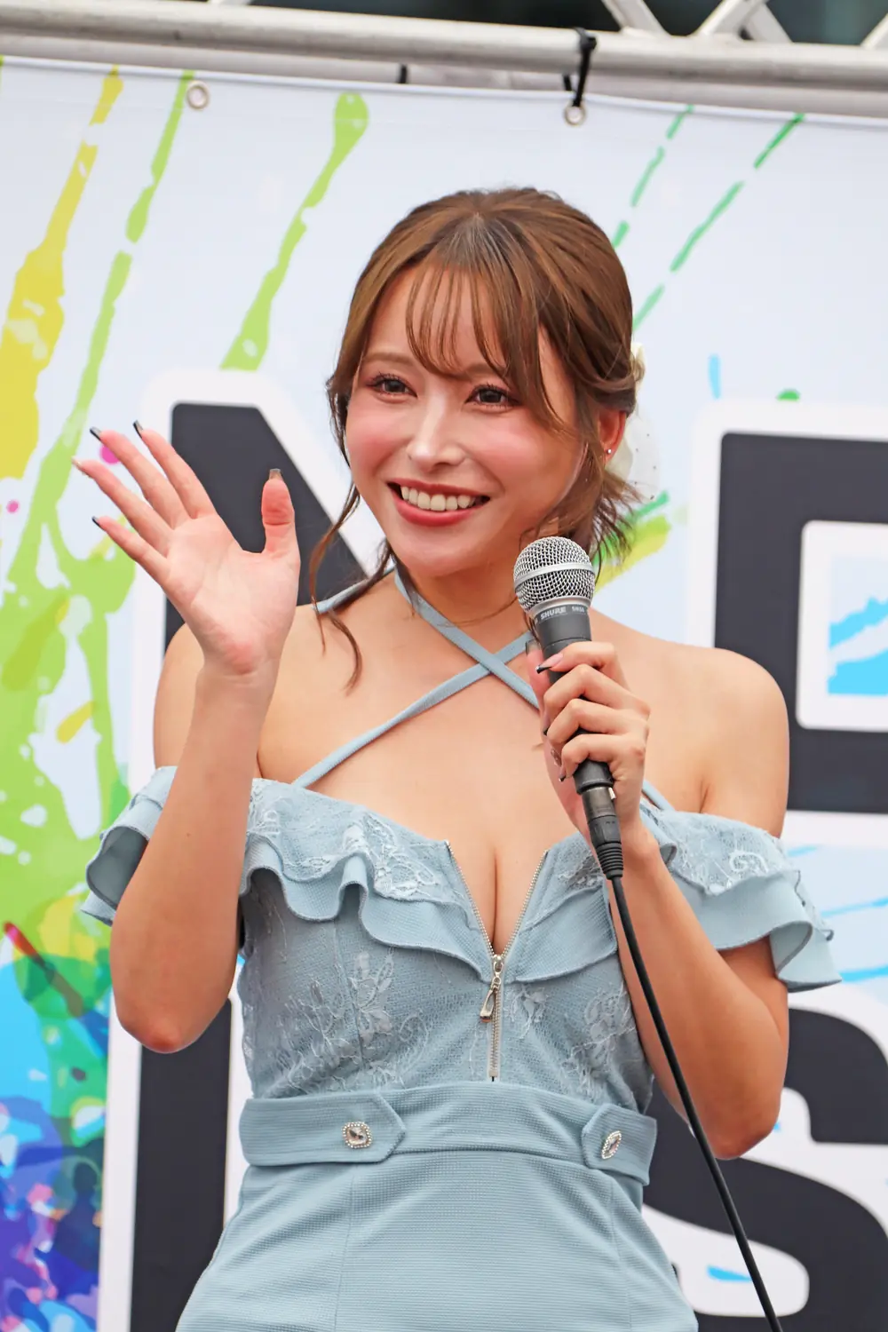 Mayuki Ito สวมชุดสีฟ้า ถือไมโครโฟนและโบกมือ