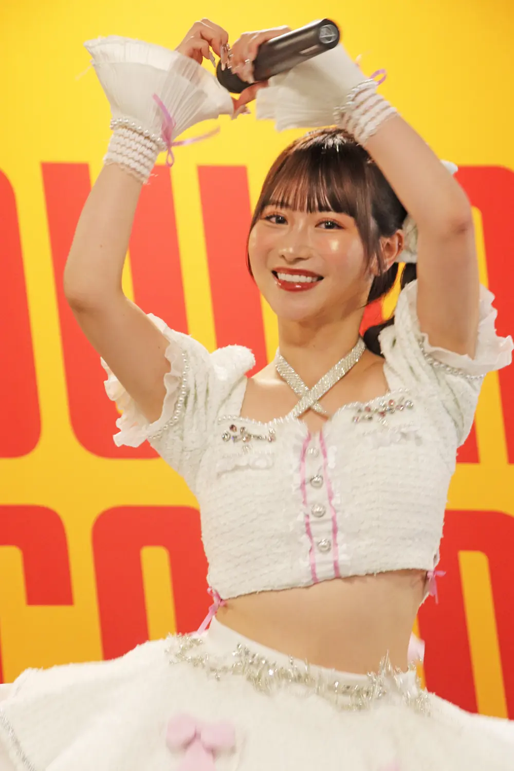 Rikka Ono สวมชุดการแสดงสีขาวและยกมือบนเวที