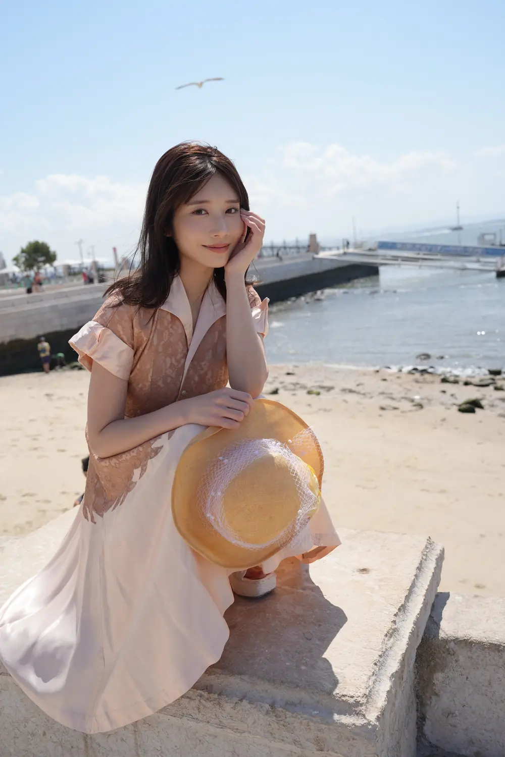 Saika Kawakita สวมเดรสสีอ่อนและถือหมวกริมทะเล