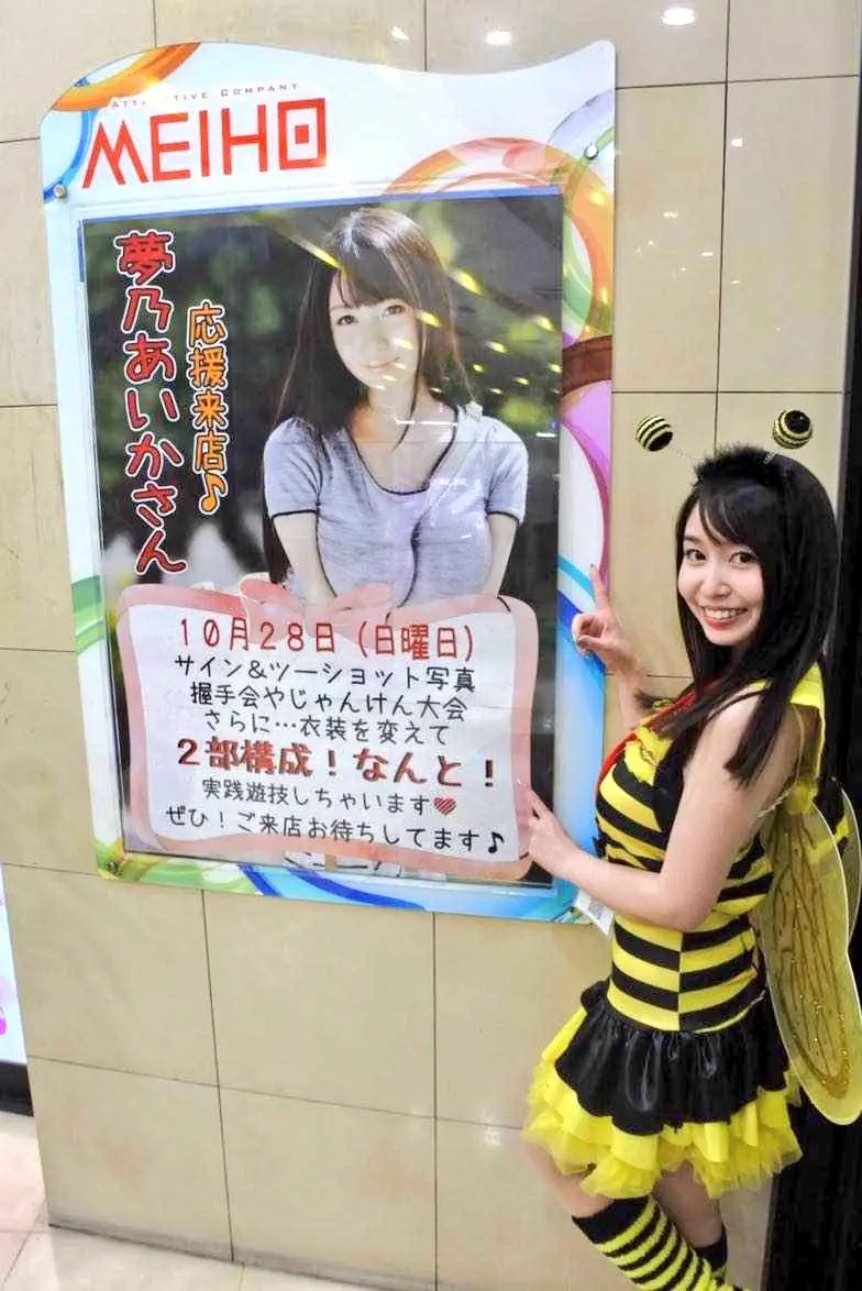 Yumeno Aika สวมชุดธีมผึ้งยืนข้างป้ายงาน MEIHO