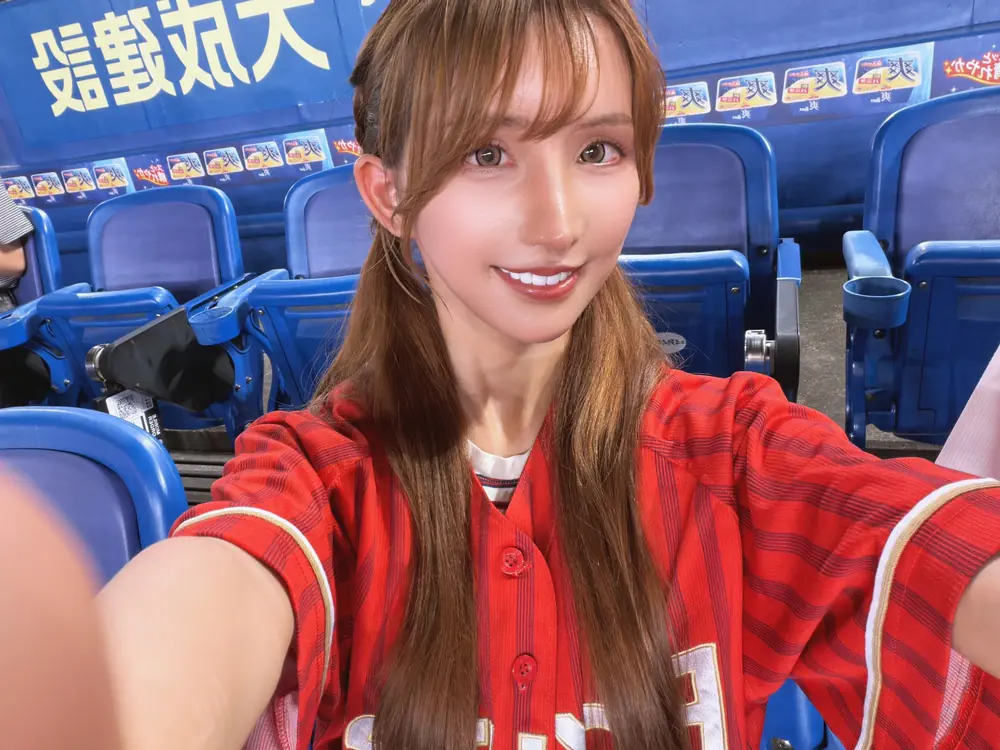 Karen Yuzuriha สวมเสื้อทีมสีแดงนั่งบนอัฒจันทร์ในสนามเบสบอล