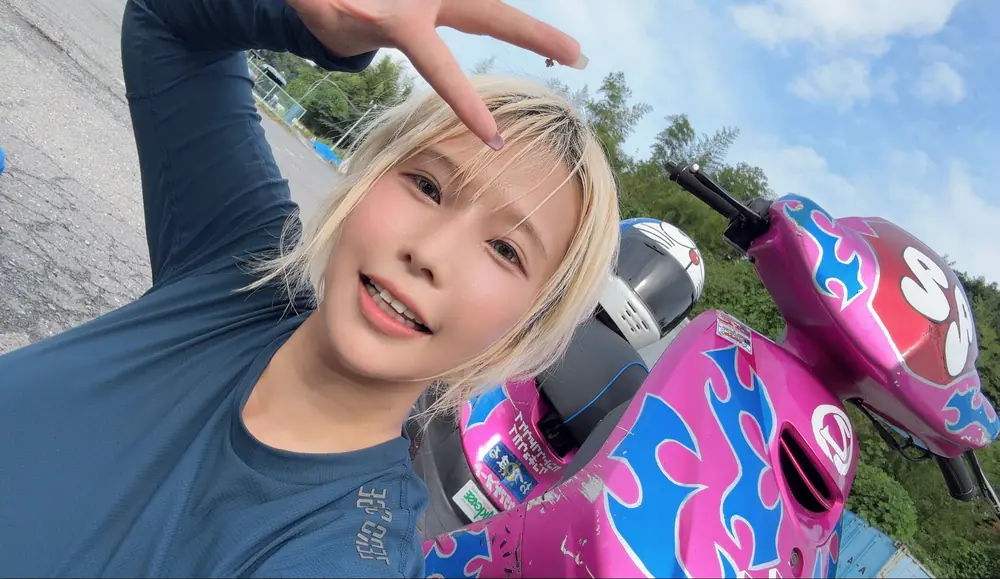 Alice Otsu ถ่ายภาพคู่กับรถสกูตเตอร์สีชมพูในสนามแข่ง