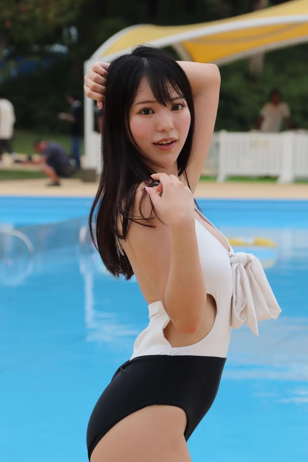 Kokoro Asano สวมชุดว่ายน้ำสีขาวดำและยกแขนข้างหนึ่งริมสระ