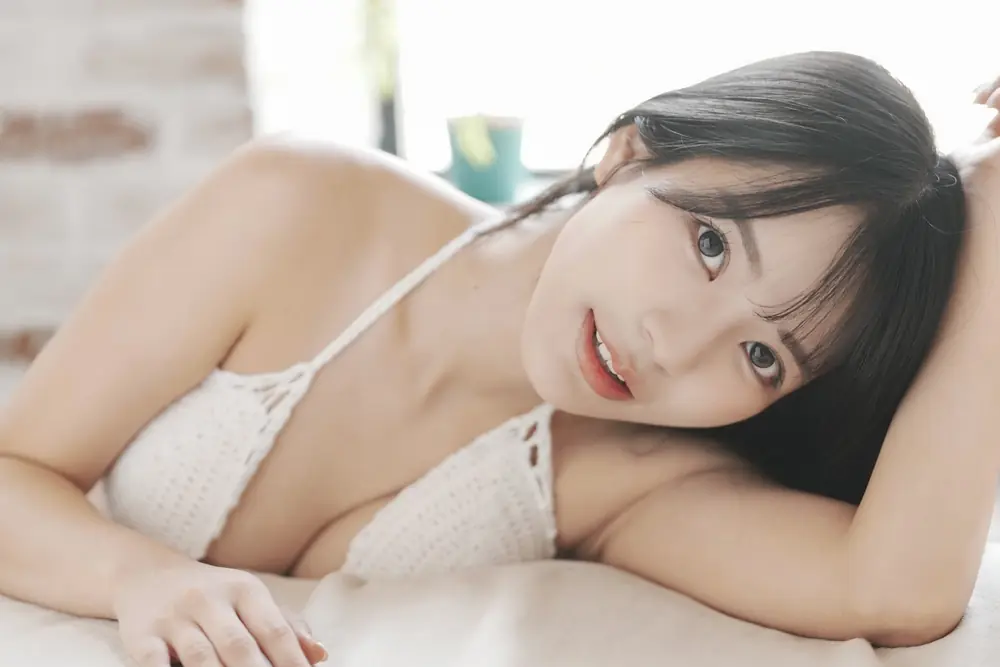 Kokoro Asano สวมชุดว่ายน้ำสีขาวและเอนตัวบนพื้นสีอ่อน