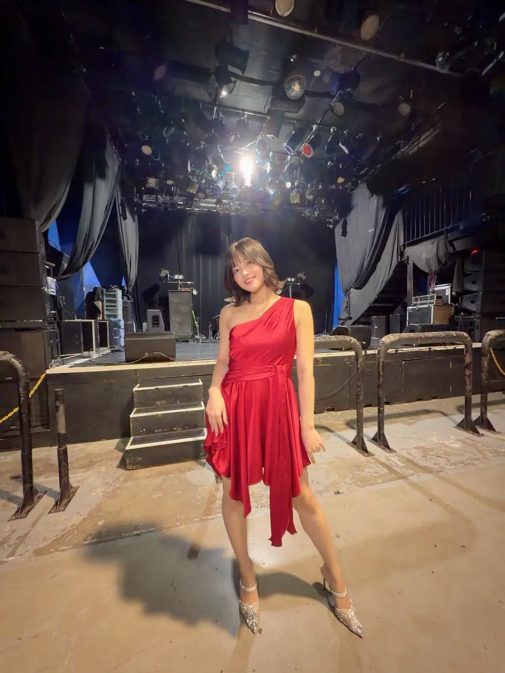 Mia Koki สวมเดรสสีแดงยืนอยู่หน้าเวทีการแสดง