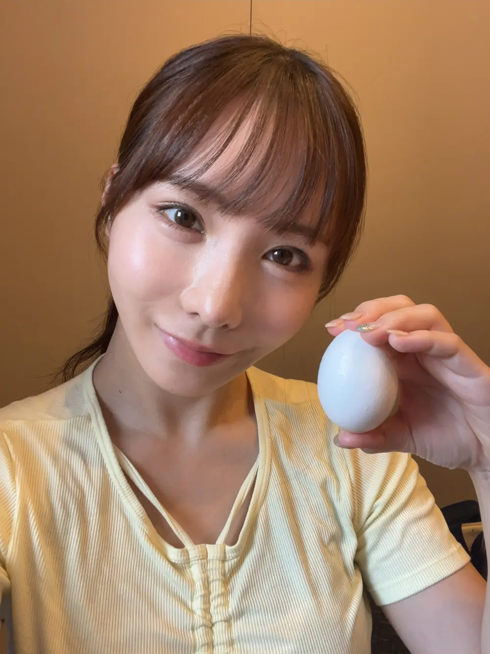 Ao Ebisaki สวมเสื้อสีเหลืองอ่อนและถือไข่ข้างใบหน้า
