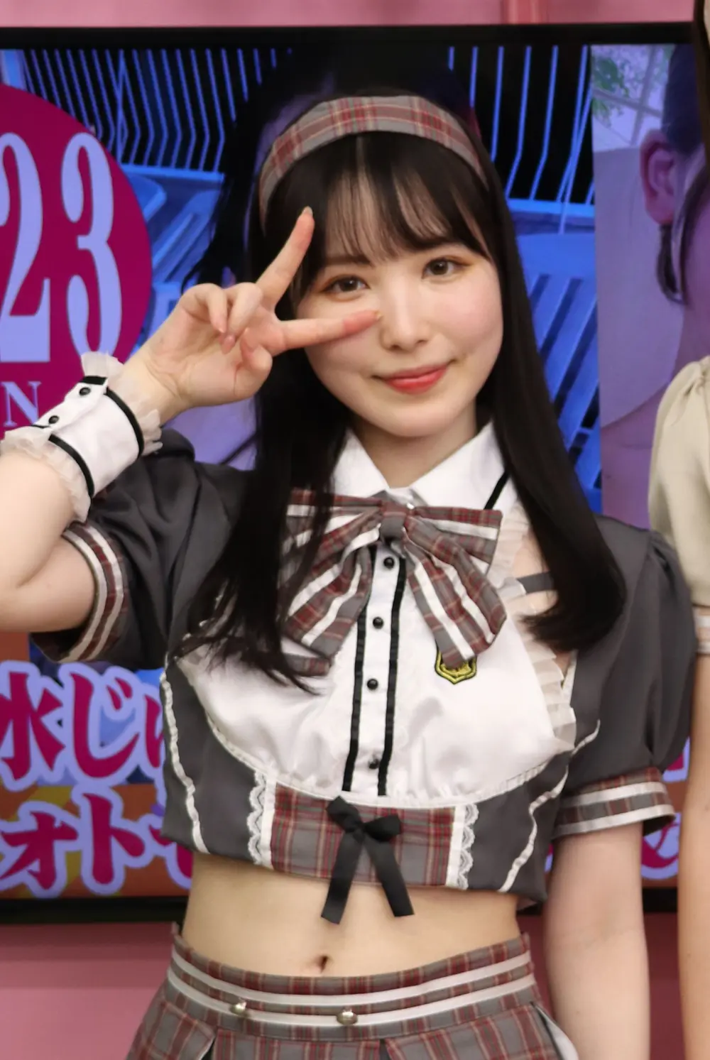 Jun Kasui สวมชุดคอสเพลย์สีเทาและโบลายตาราง พร้อมชูสองนิ้ว