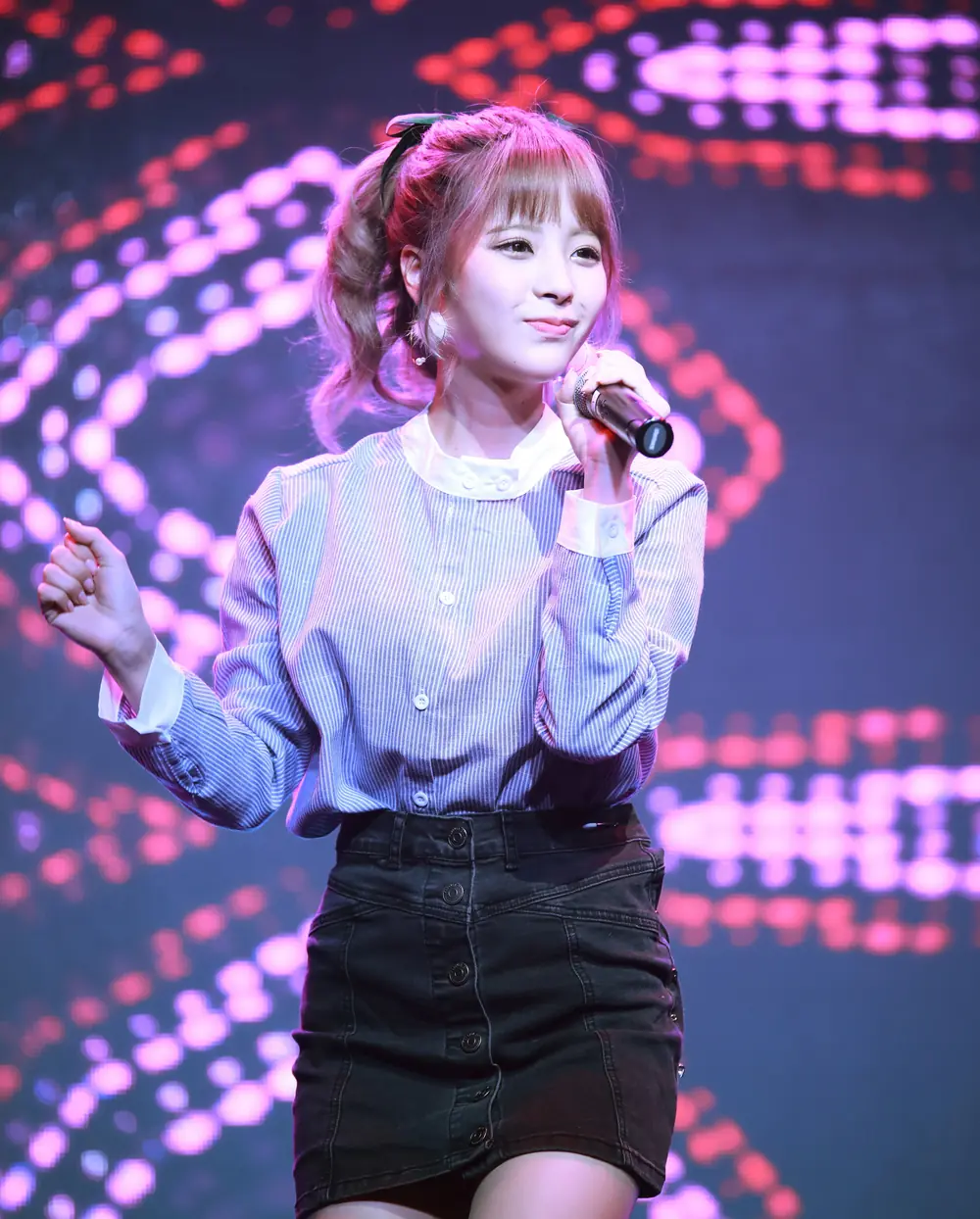 Kana Momonogi สวมเสื้อลายทางและกระโปรงสีดำ ถือไมโครโฟนบนเวที