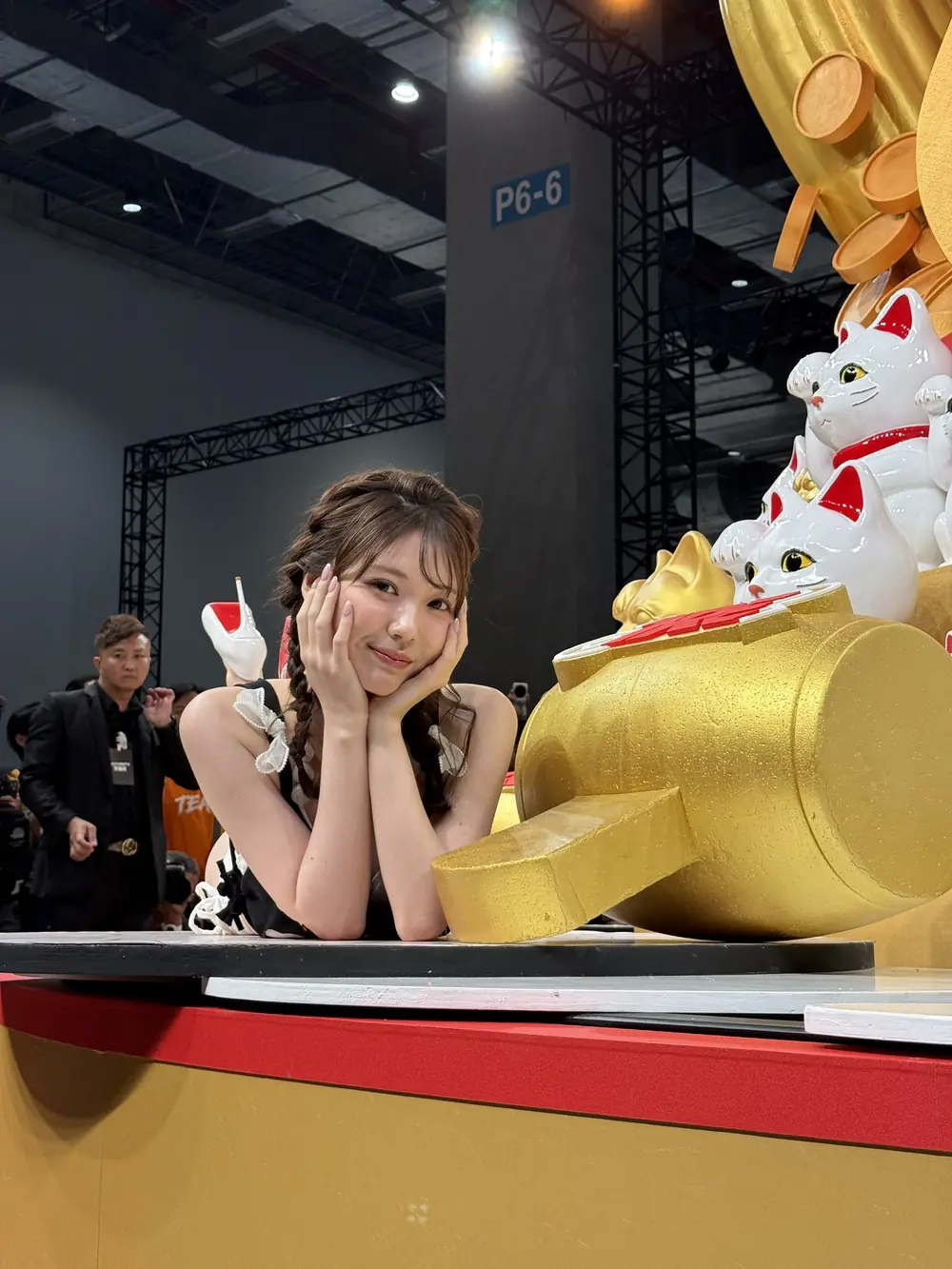 Mio Ishikawa ถักผมเปียและวางมือข้างแก้มข้างรูปปั้นแมวกวักสีทองในงาน