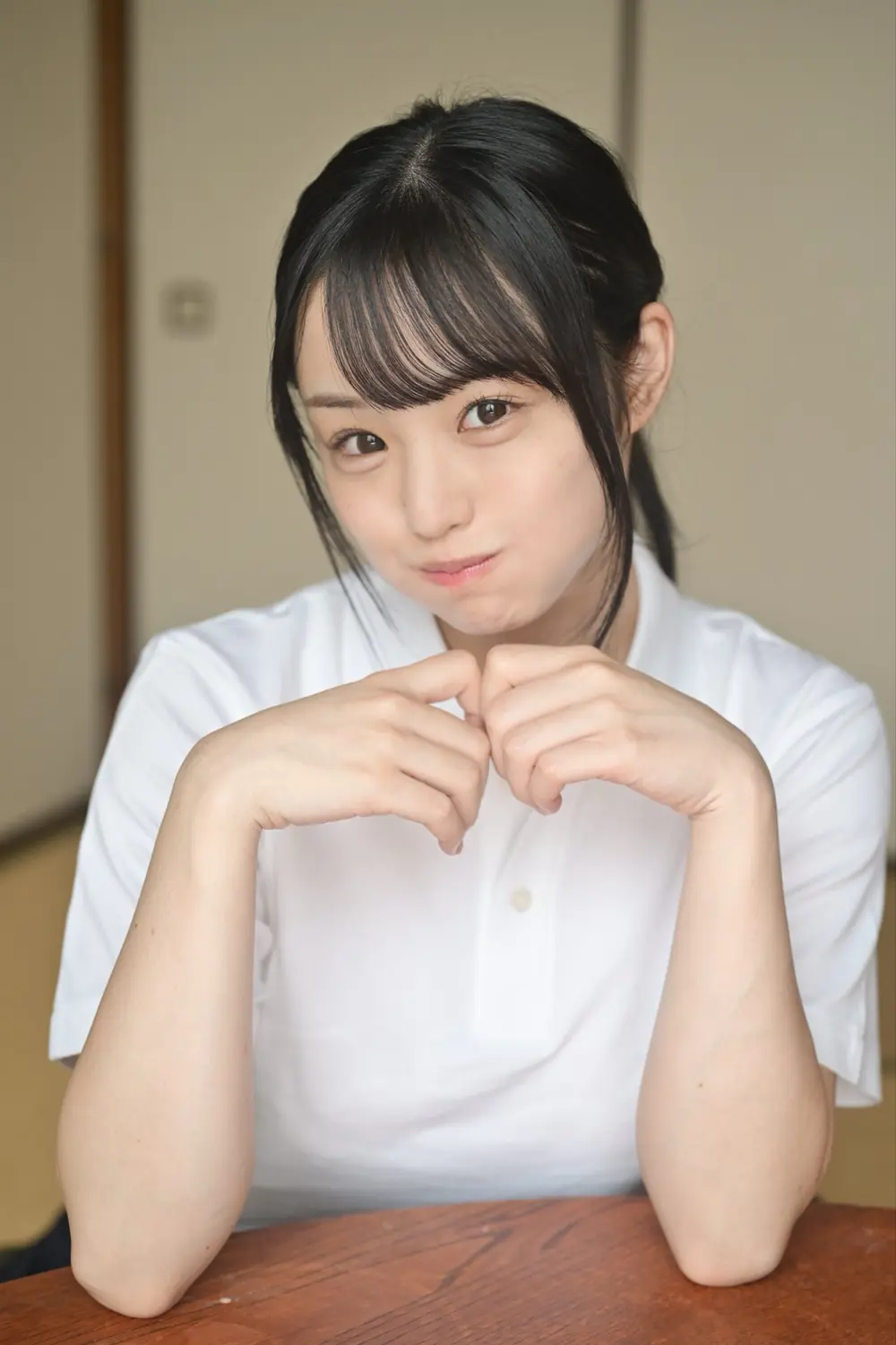 Yoru Tsukumo สวมเสื้อสีขาว วางแขนบนโต๊ะและทำแก้มป่อง