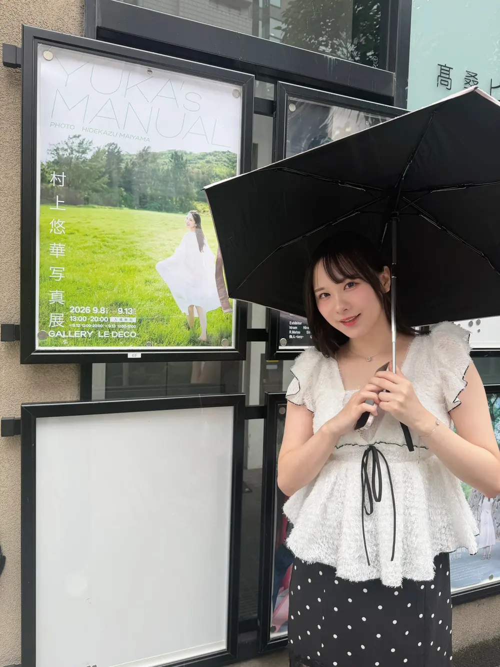 Yuka Murakami ยืนถือร่มหน้าสถานที่จัดนิทรรศการภาพถ่าย
