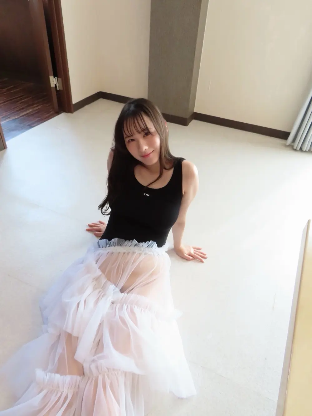 Yuka Murakami สวมเสื้อสีดำกับกระโปรงยาวสีขาวนั่งบนพื้นห้อง