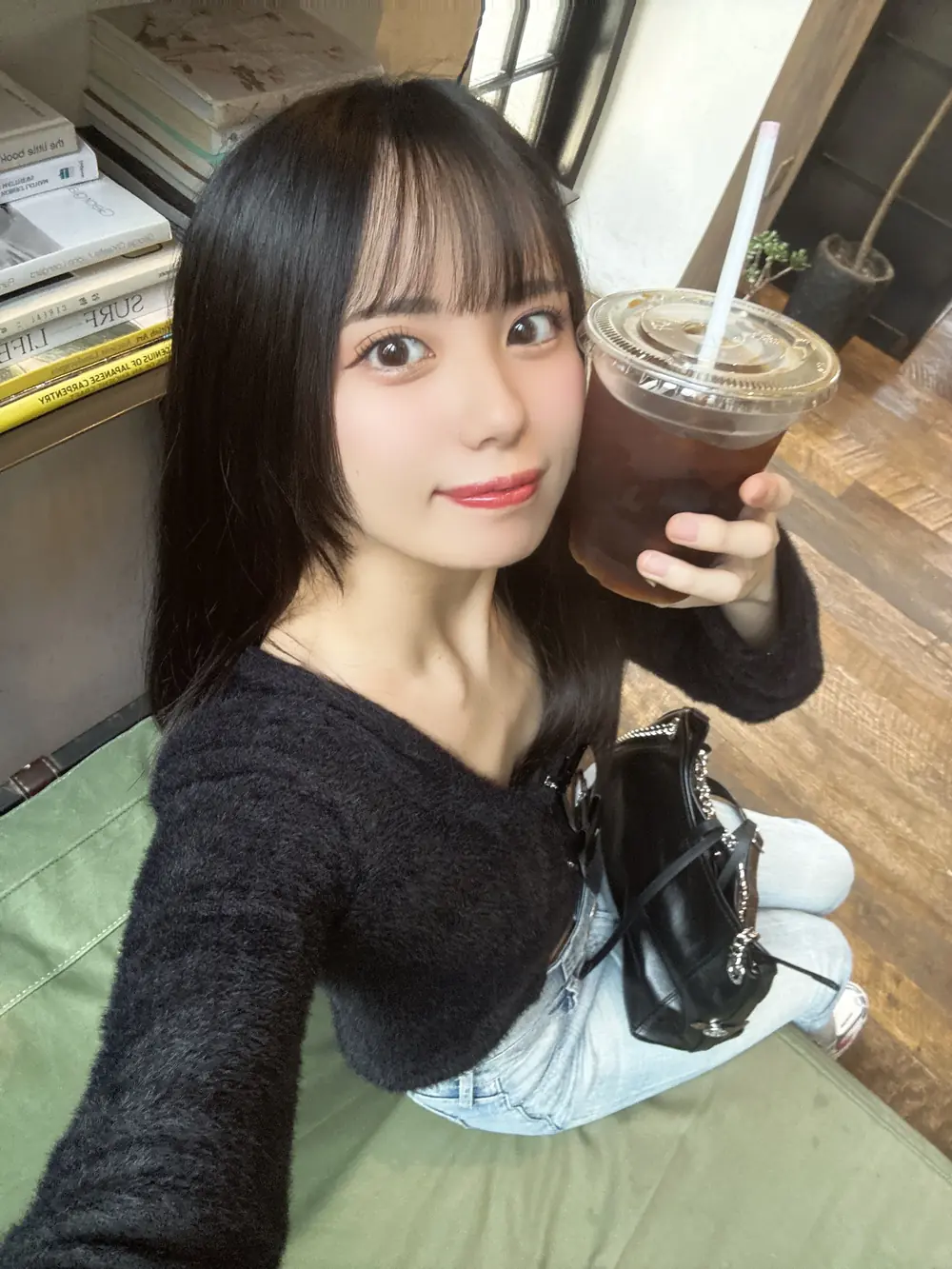 Airi Nagisa สวมเสื้อสีดำและถือแก้วเครื่องดื่มในคาเฟ่