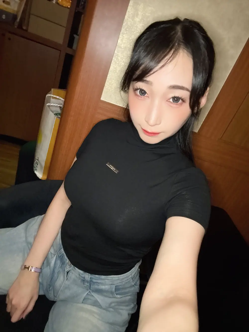 Kurea Hasumi สวมเสื้อสีดำและกางเกงยีนส์ถ่ายภาพในห้อง