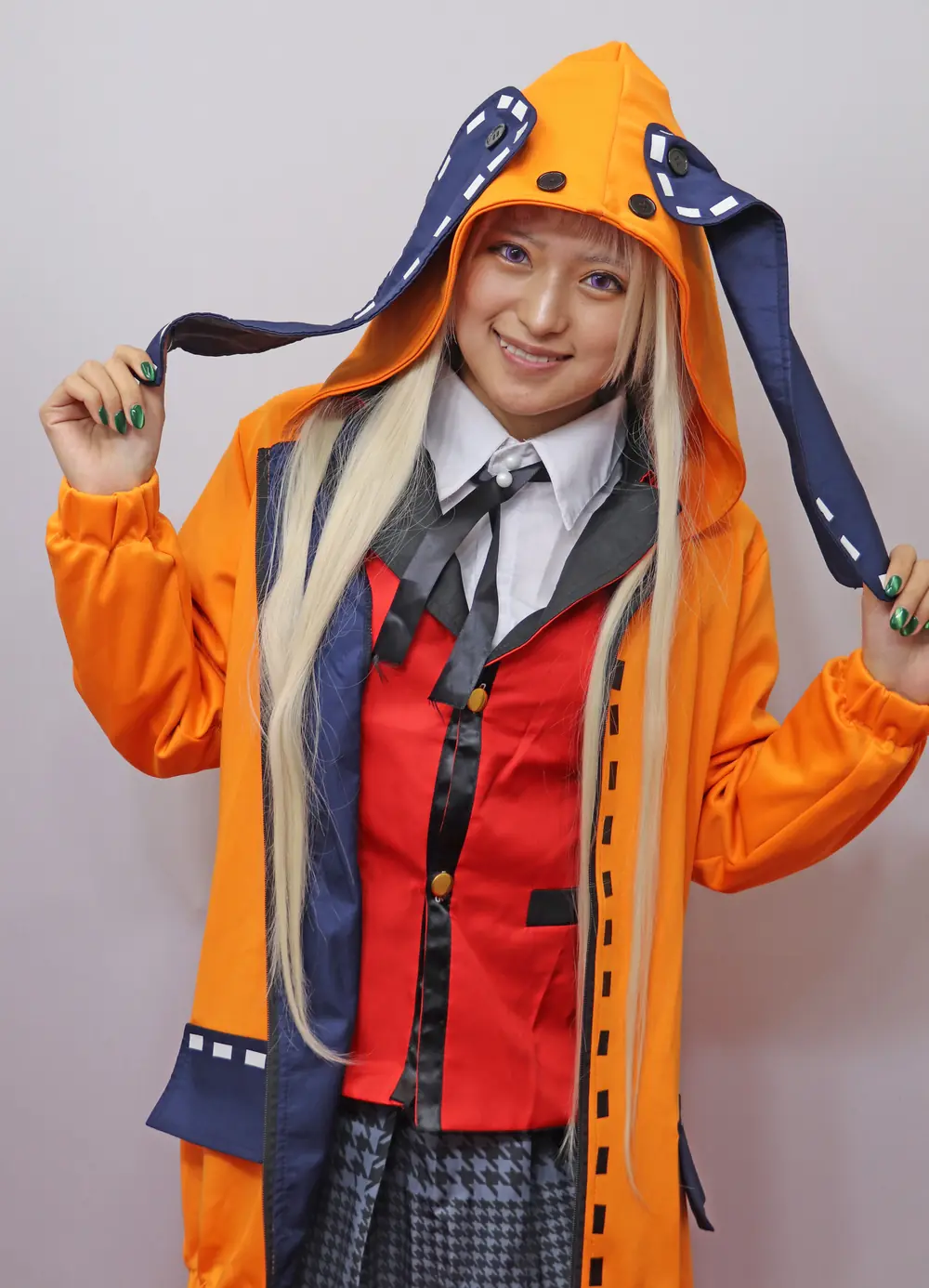 Mitsuki Nagisa สวมเสื้อคลุมมีฮู้ดสีส้มทับชุดคอสเพลย์สีแดงและดำ