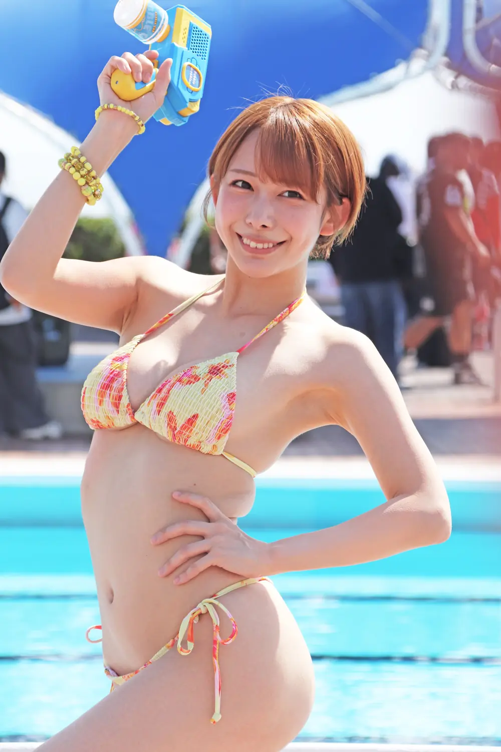 Mizuki Yayoi ยิ้มและถือปืนฉีดน้ำสีฟ้าเหลืองริมสระ