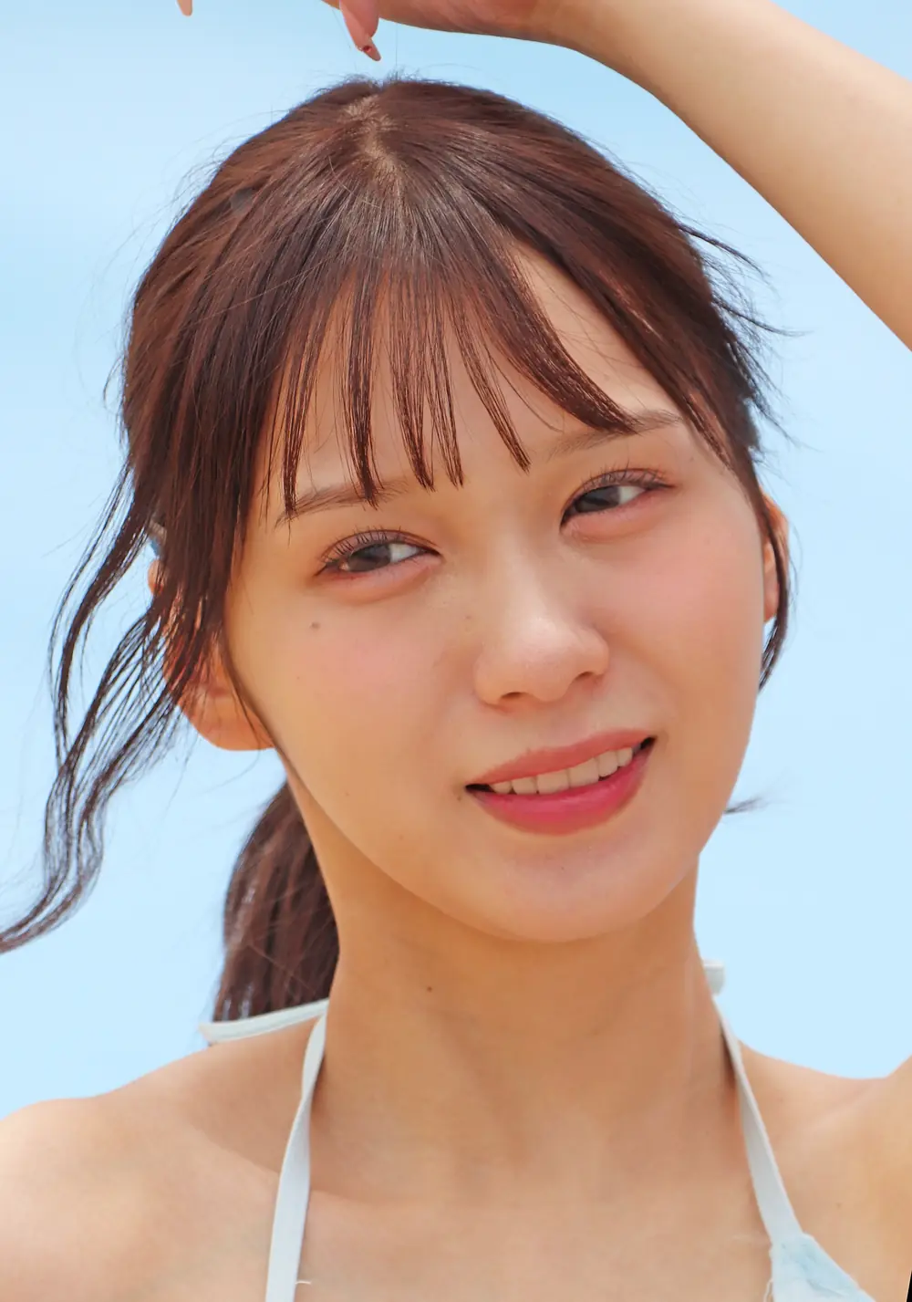 Nanami Kodama ยิ้มให้กล้องและยกแขนเหนือศีรษะกลางแจ้ง