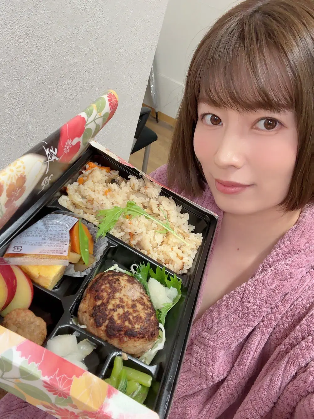 Saki Okuda สวมเสื้อคลุมสีชมพูและถือกล่องอาหาร