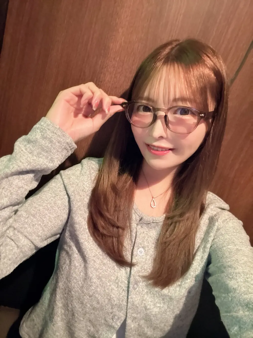 China Chisaki สวมเสื้อคาร์ดิแกนสีเทาและแว่นตา ยกมือจับกรอบแว่น