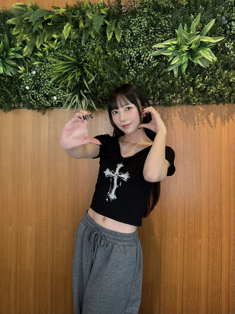 Mia Nanasawa สวมเสื้อสีดำและกางเกงสีเทาหน้าผนังประดับใบไม้