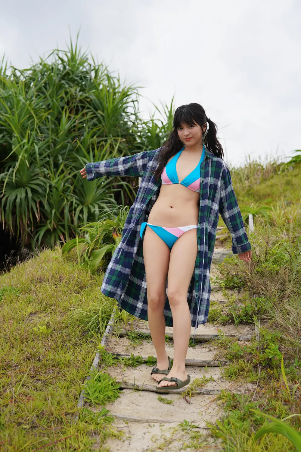 Akari Neo สวมชุดว่ายน้ำสีฟ้าและเสื้อคลุมลายสก็อตบนทางเดินกลางแจ้ง