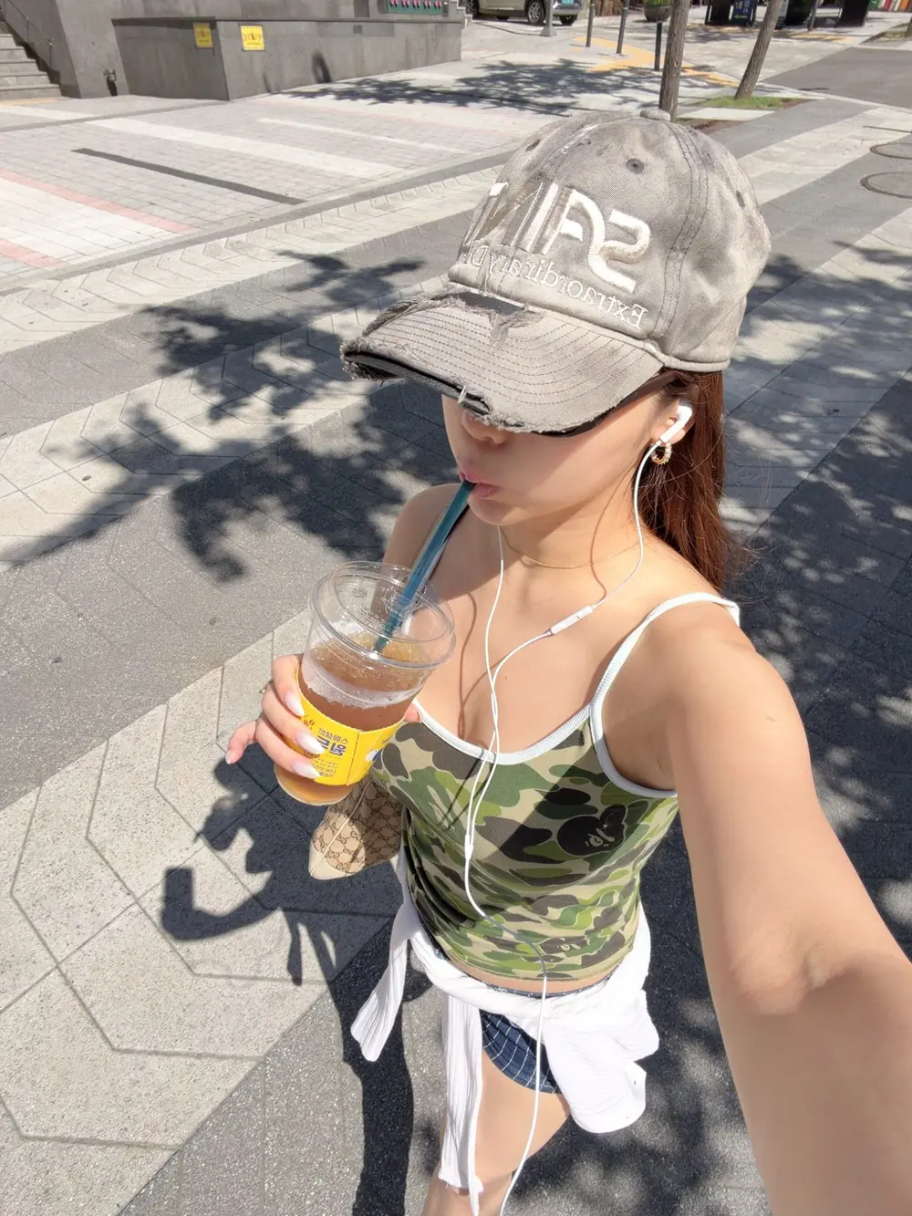 Yuki Yoshizawa สวมหมวกแก๊ปและเสื้อสีเขียวถือแก้วเครื่องดื่มกลางแจ้ง