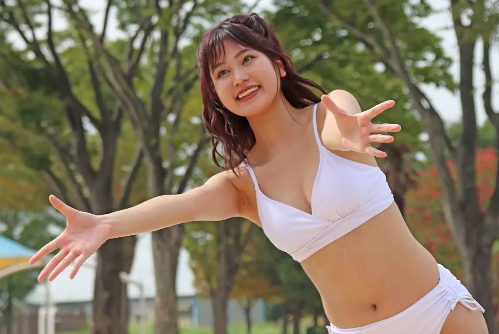 Maeda Minami สวมชุดว่ายน้ำสีขาว ยิ้มและกางแขนกลางแจ้ง