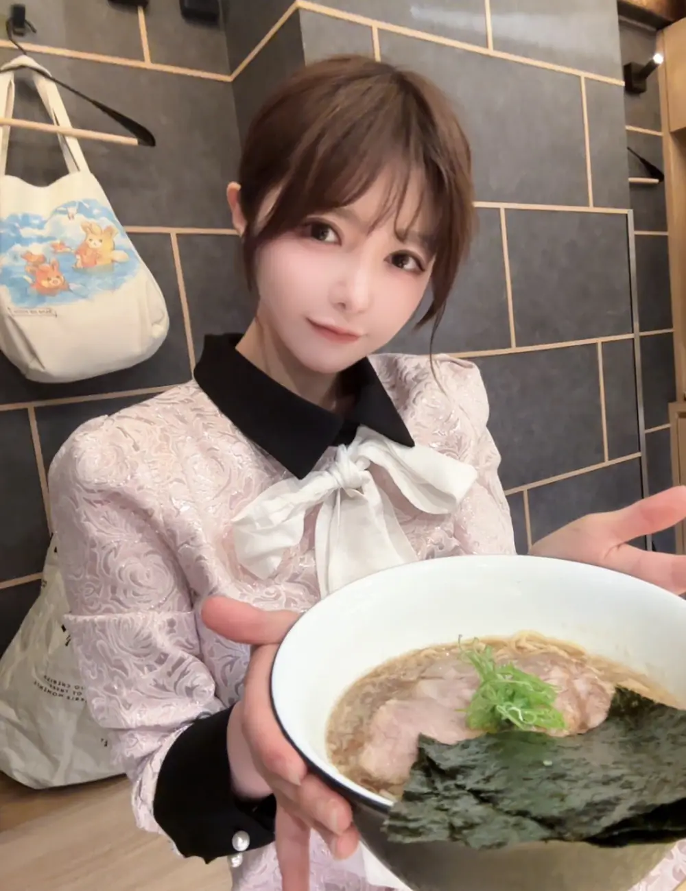 Mami Zenba สวมเสื้อสีอ่อนผูกโบและถือชามราเมง