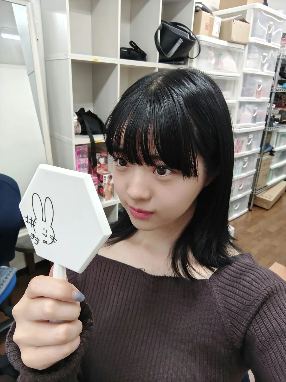 Momo Inoue สวมเสื้อสีน้ำตาลถือกระจกด้ามจับสีขาว