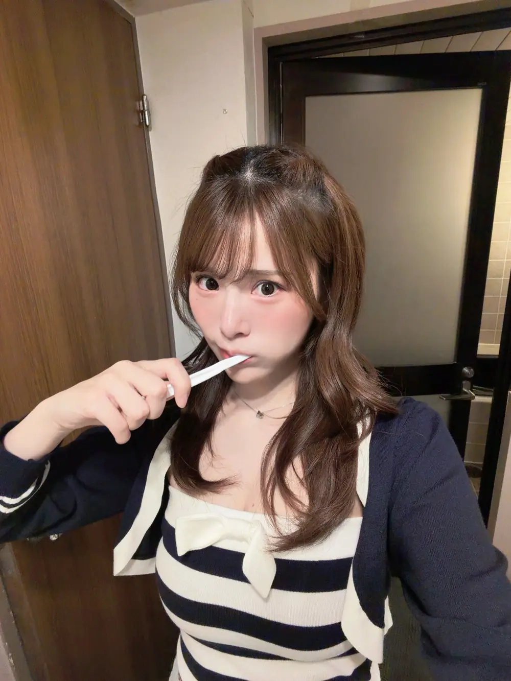 Nano Ogasawara สวมเสื้อลายทางและคาร์ดิแกนสีเข้มขณะแปรงฟัน