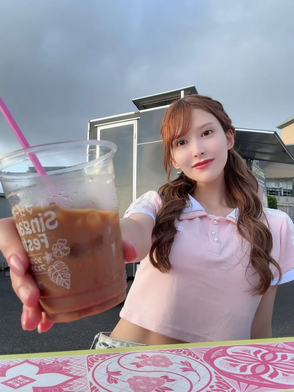 Ranran Fujii สวมเสื้อสีชมพูยื่นแก้วเครื่องดื่มหน้าโต๊ะกลางแจ้ง