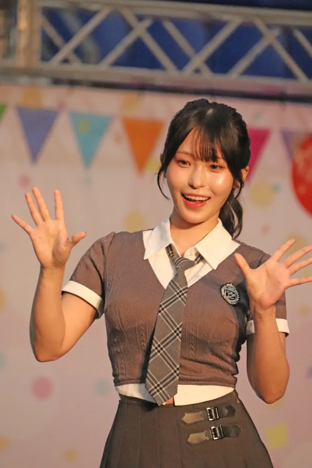 Sora Arakawa สวมเสื้อสีเทากับเนกไทลายตาราง ยกมือทักทายบนเวที