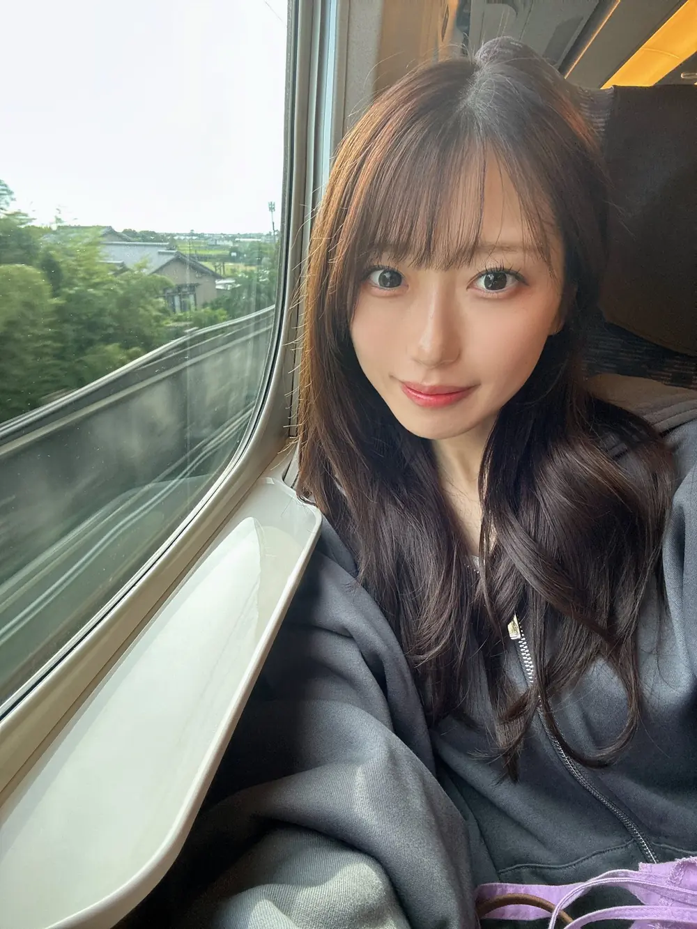 Ui Amagami สวมเสื้อสีเข้มนั่งข้างหน้าต่างรถไฟ