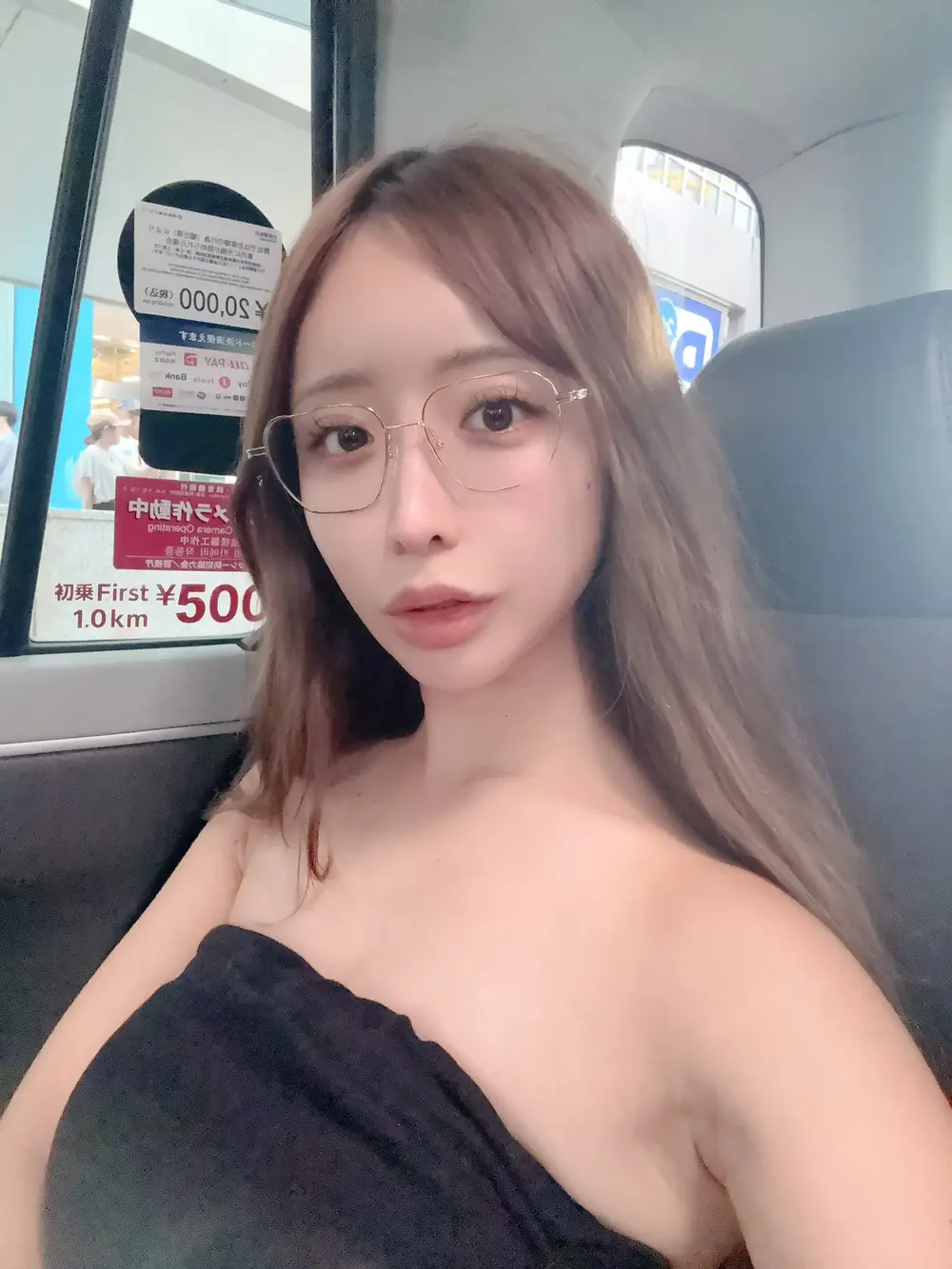 Mio Hanasaki สวมแว่นกรอบโลหะและเสื้อเกาะอกสีดำขณะนั่งในรถ