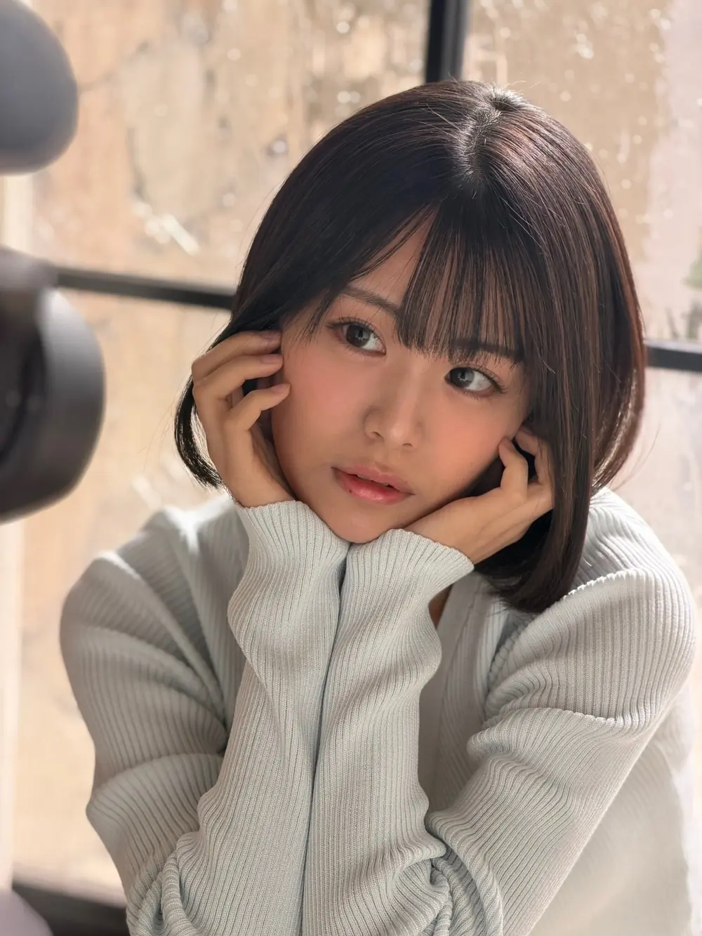 Sara Asahina สวมเสื้อแขนยาวสีเทาอ่อนและวางมือข้างใบหน้า