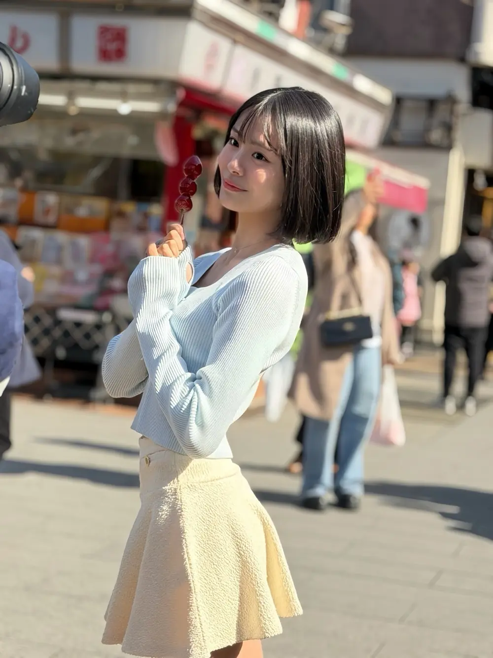 Sara Asahina สวมเสื้อสีฟ้าอ่อนและกระโปรงสีเหลืองถือขนมบนถนน