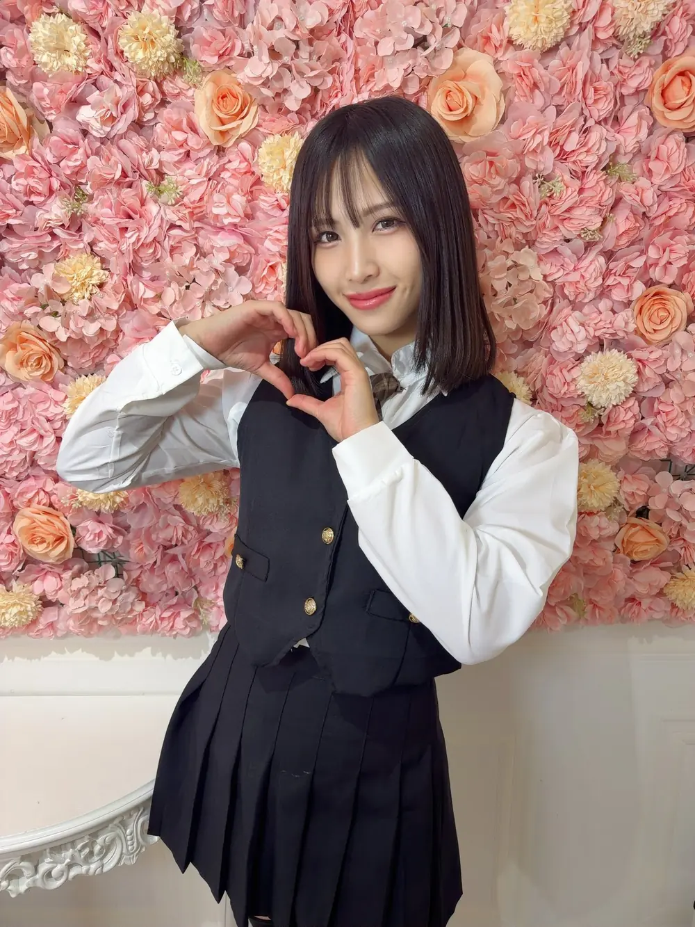 Aya Nanjo สวมเสื้อเชิ้ตสีขาวกับเสื้อกั๊กสีดำหน้าฉากดอกไม้