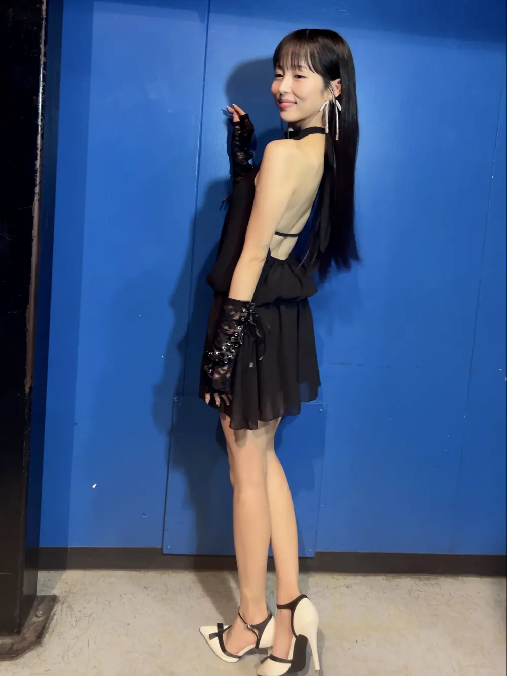 Hana Honjo สวมชุดสีดำและรองเท้าส้นสูงหน้าผนังสีน้ำเงิน