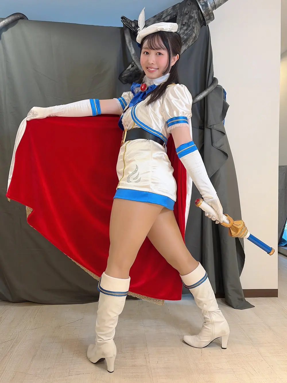 Machi Ikuno สวมชุดคอสตูมสีขาวน้ำเงินพร้อมดาบ ยืนยิ้มในฉากงาน
