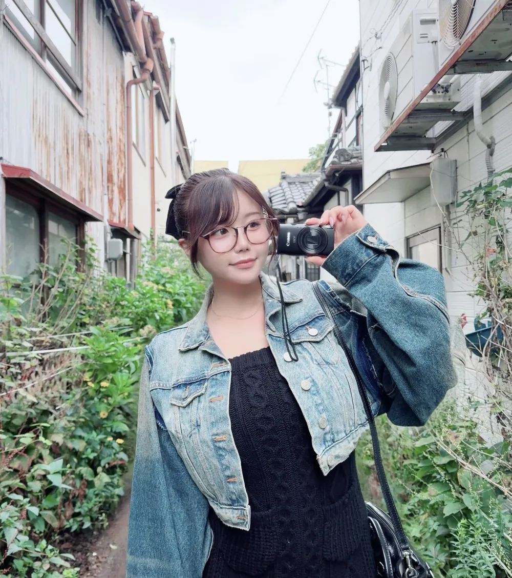 Miu Mirai สวมแว่นและแจ็กเก็ตยีนส์ถือกล้องในตรอกย่านบ้านพัก