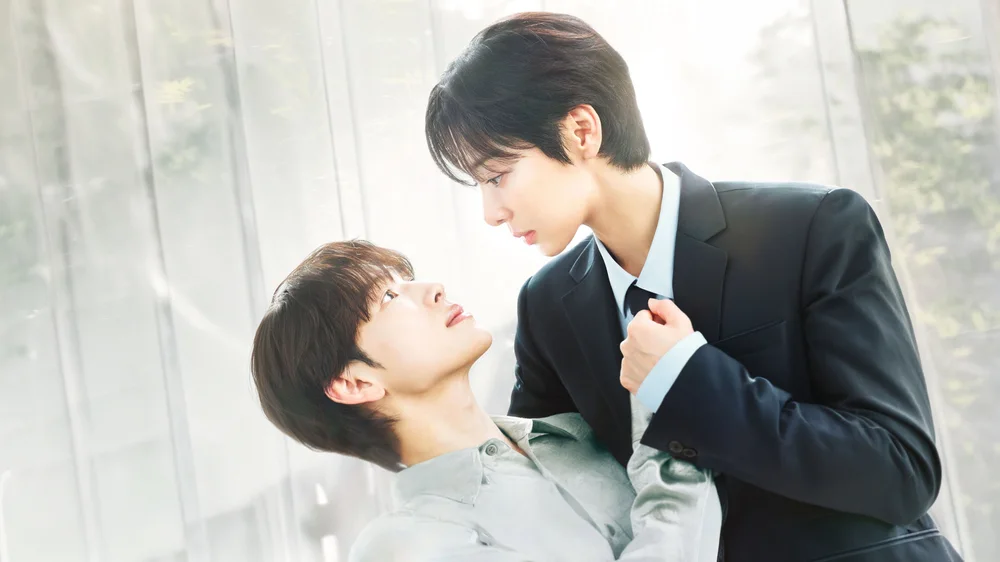 ตัวละครนำสองคนยืนใกล้กันในห้องสว่าง ฝ่ายหนึ่งกำเนกไทของอีกฝ่าย