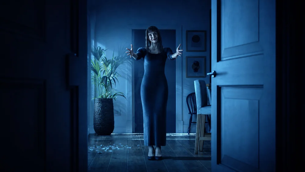 หญิงสาวยืนกางแขนในโถงทางเดินที่จัดแสงสีฟ้าเข้ม มีเศษกระดาษกระจายบนพื้น