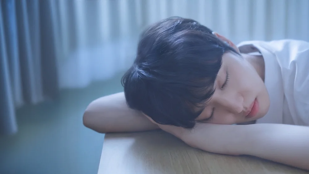 ชายคนหนึ่งนอนหลับซบแขนบนโต๊ะในแสงโทนเย็น