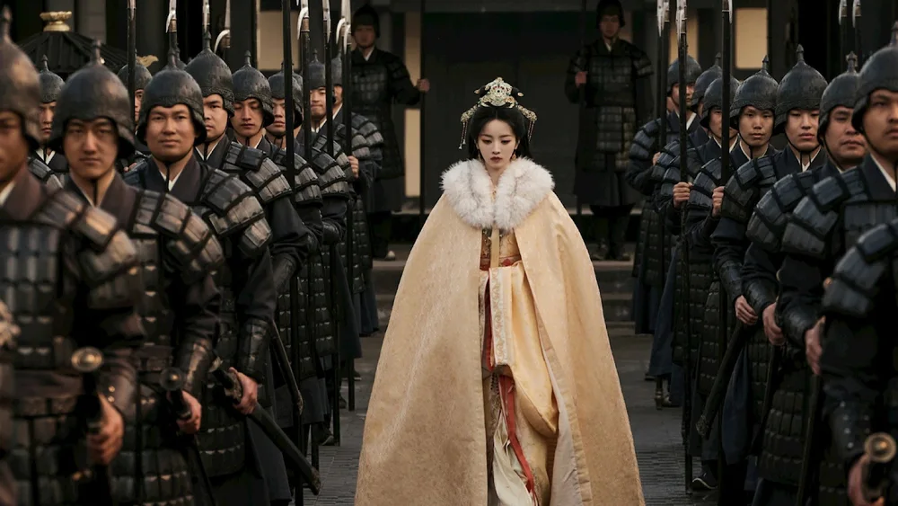 ภาพจากซีรีส์ หญิงสาวสวมผ้าคลุมขนสีครีมเดินผ่านแถวทหารที่สวมเกราะถืออาวุธ
